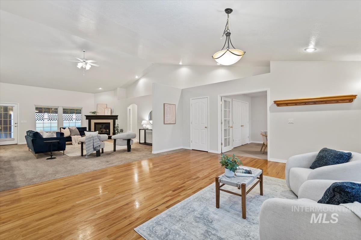Living room featuring vaulted ceiling, light wood-style flooring, ceiling fan, and a glass covered fireplace