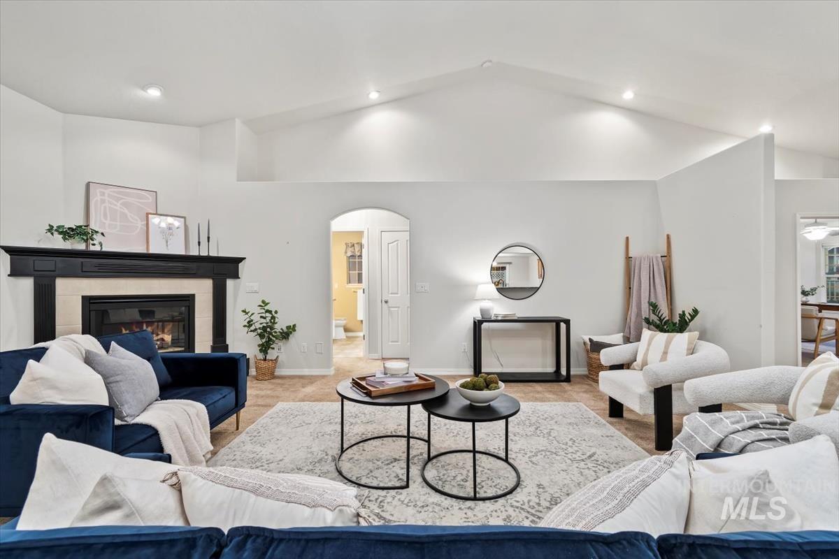 Carpeted living room with vaulted ceiling, a tiled fireplace, arched walkways, and recessed lighting