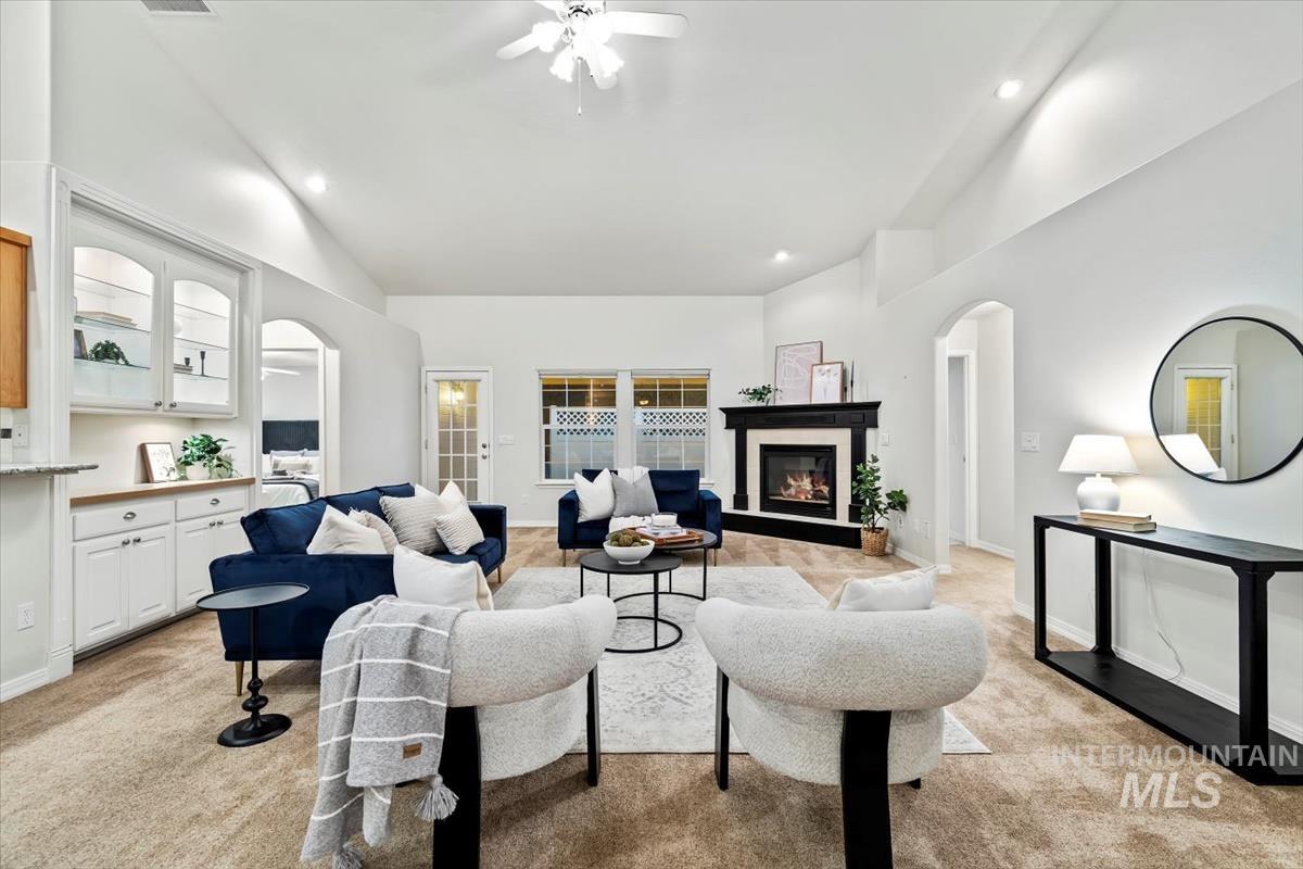 Living room with arched walkways, light carpet, a glass covered fireplace, recessed lighting, and a ceiling fan