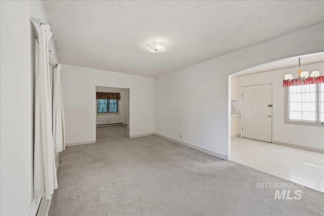 Carpeted empty room featuring a textured ceiling, arched walkways, and baseboard heating
