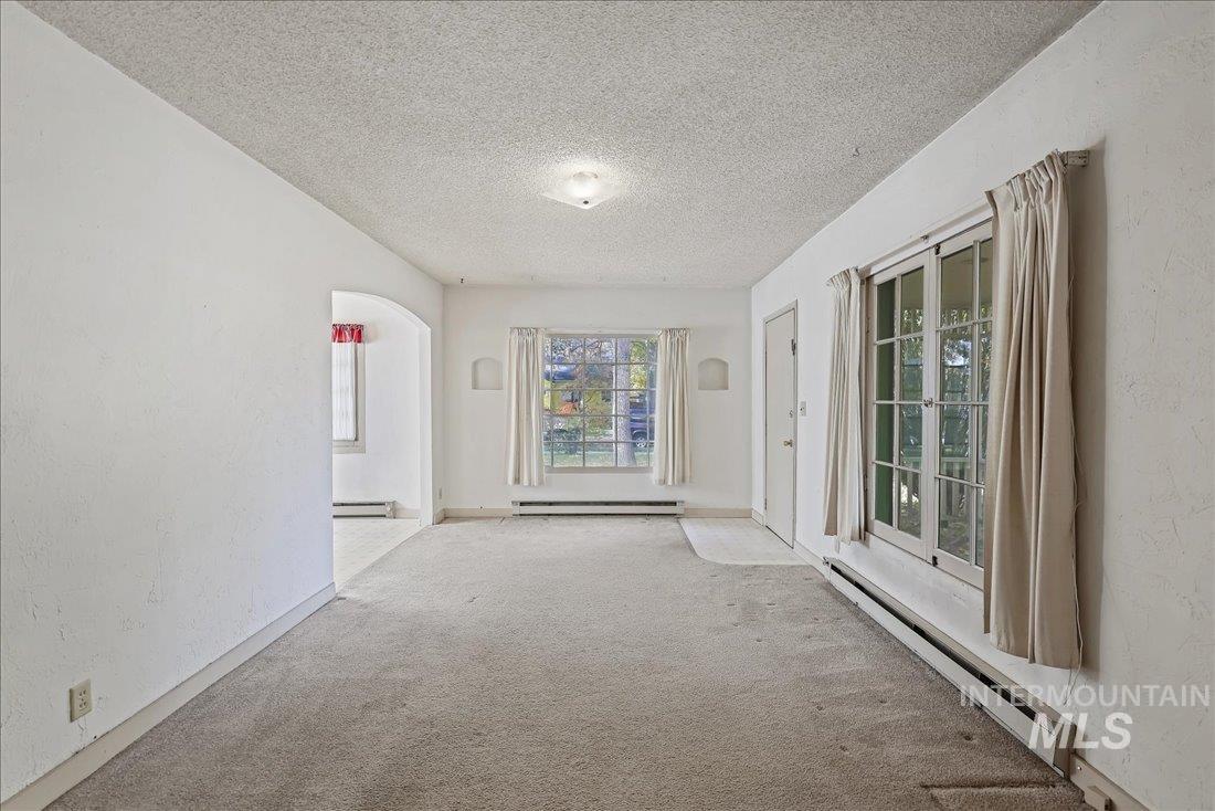 Carpeted spare room featuring a baseboard heating unit, a textured wall, a textured ceiling, arched walkways, and baseboard heating