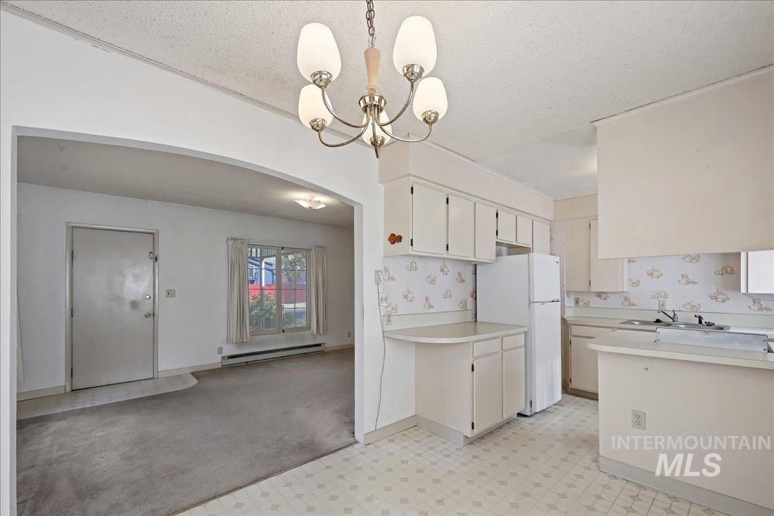 Kitchen featuring a textured ceiling, light countertops, freestanding refrigerator, light flooring, and arched walkways