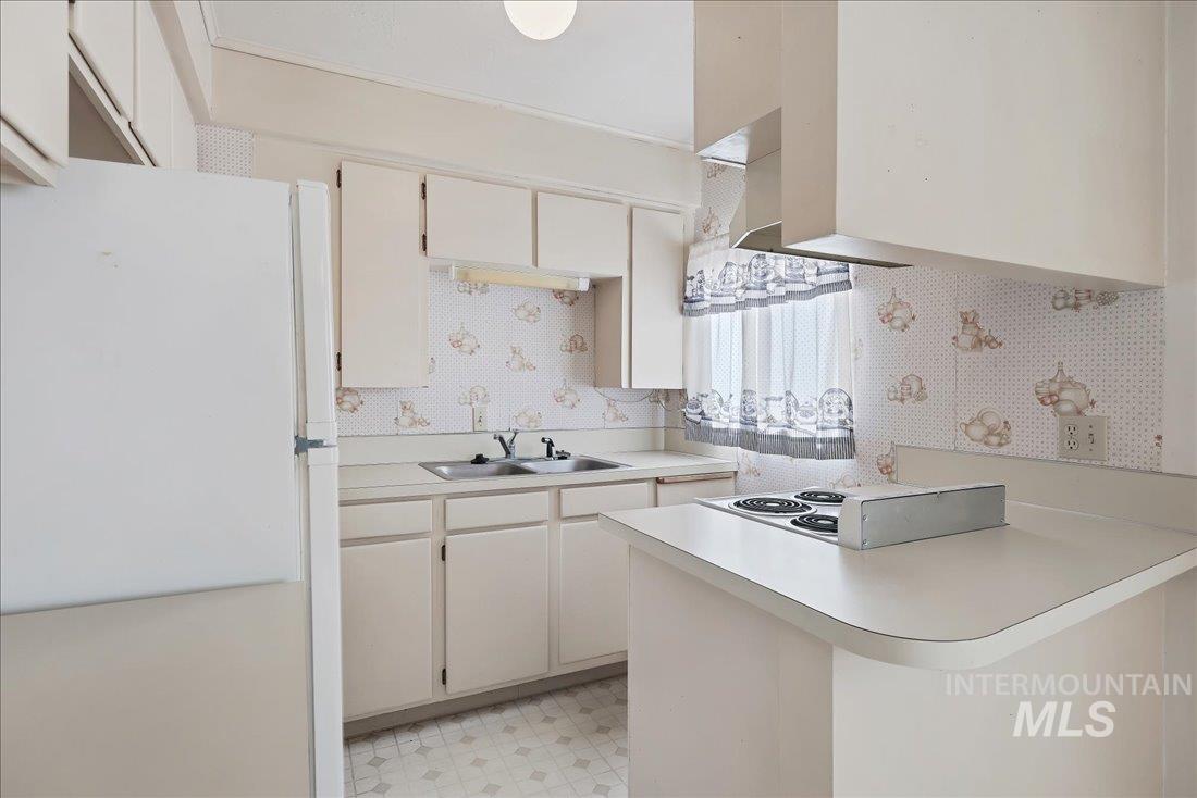 Kitchen featuring white appliances, light countertops, a peninsula, light floors, and wallpapered walls