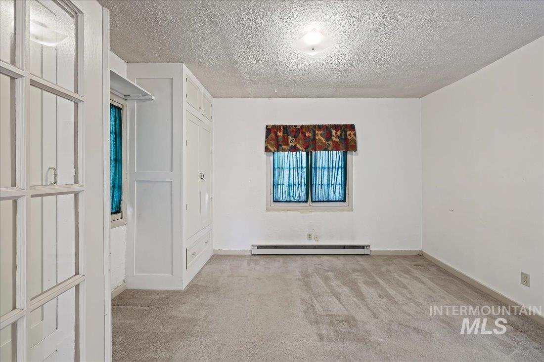 Spare room with light colored carpet, a textured ceiling, and baseboard heating