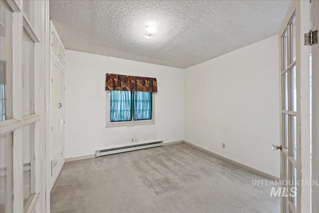 Spare room featuring french doors, a baseboard radiator, light carpet, and a textured ceiling