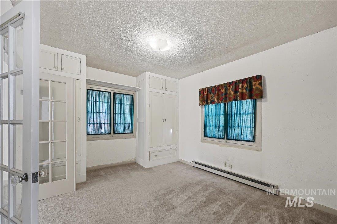 Unfurnished room with a baseboard radiator, light colored carpet, a textured ceiling, french doors, and a textured wall
