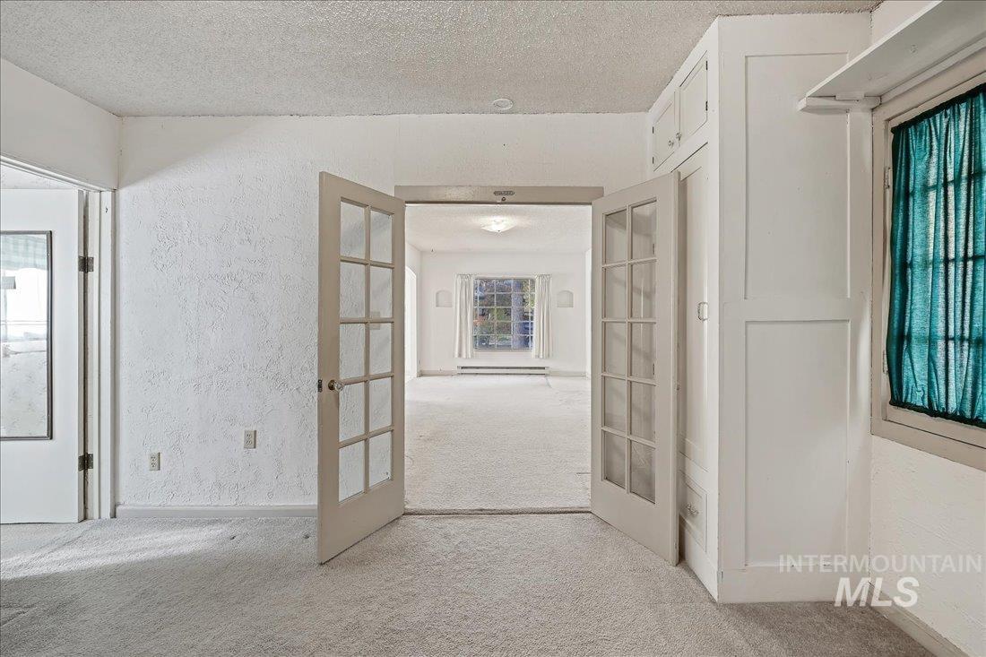 Hallway featuring french doors, a textured wall, carpet flooring, and a textured ceiling
