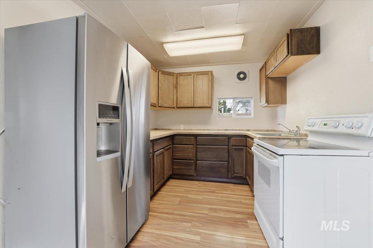Kitchen with stainless steel fridge with ice dispenser, white range with electric cooktop, light countertops, light wood-type flooring, and washer / dryer