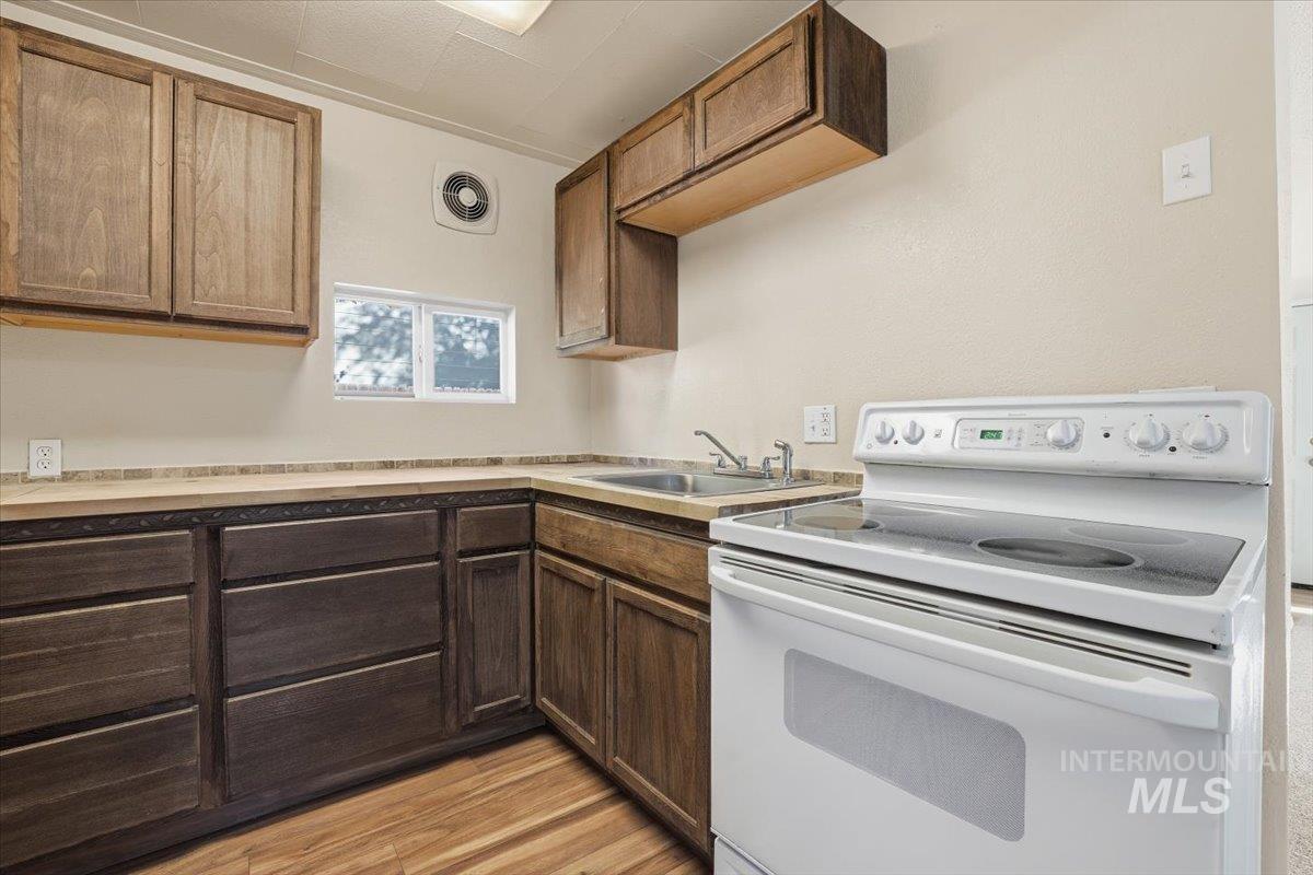 Kitchen featuring white electric stove, light countertops, light wood-style floors, and dark brown cabinetry