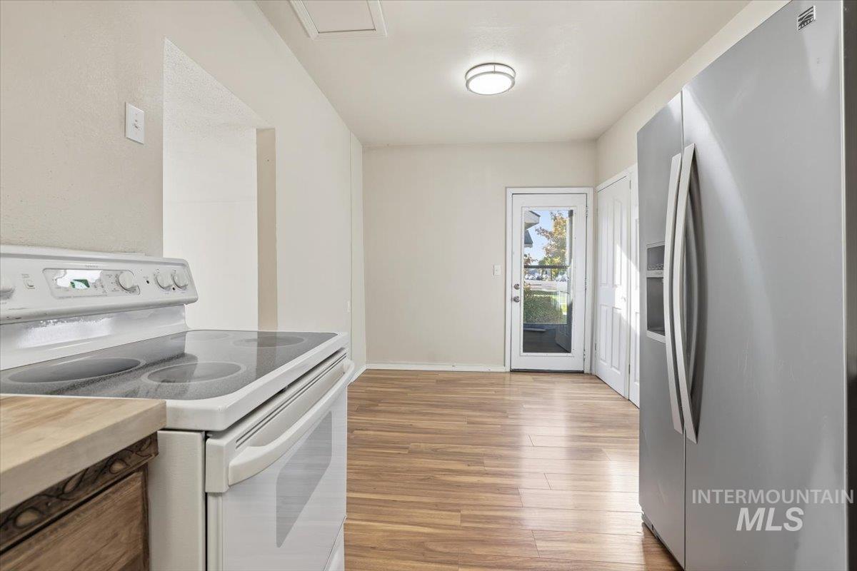 Kitchen with white range with electric stovetop, stainless steel fridge, light wood finished floors, and butcher block countertops