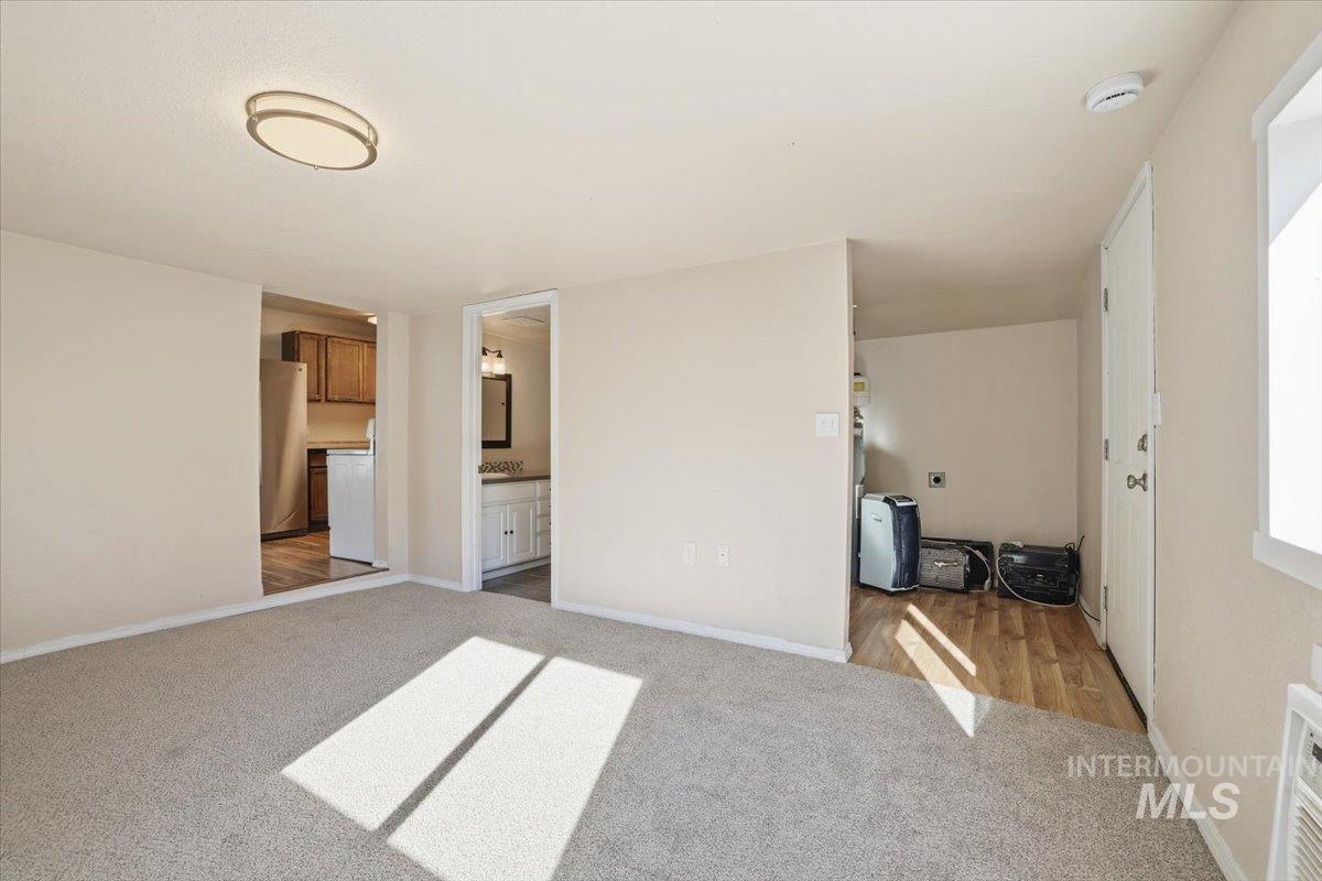 Unfurnished bedroom featuring light carpet, connected bathroom, and freestanding refrigerator