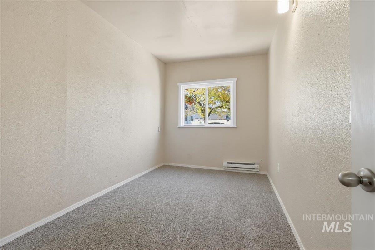 Carpeted empty room with a textured wall and a baseboard radiator