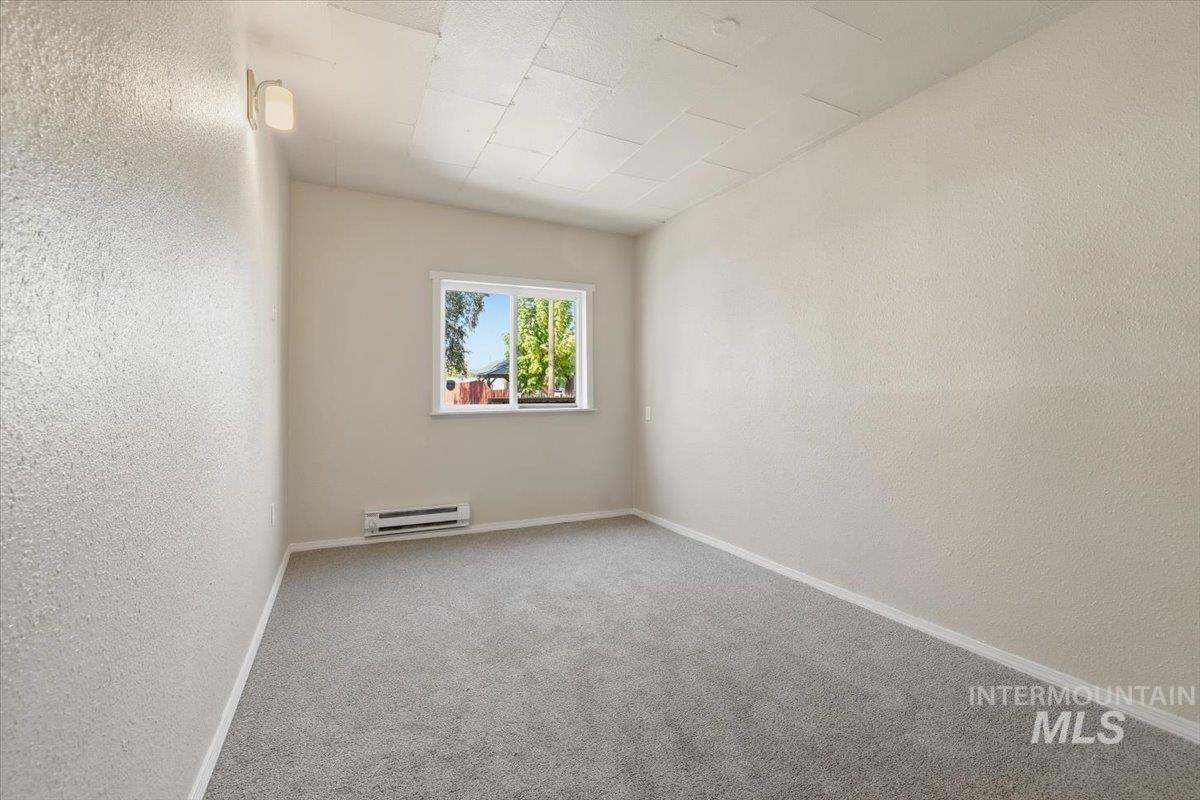 Carpeted empty room with a textured wall and baseboard heating