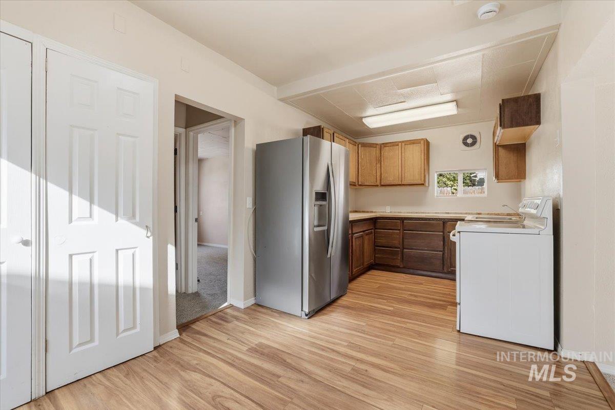 Kitchen featuring stainless steel refrigerator with ice dispenser, light countertops, light wood-style floors, white range with electric cooktop, and brown cabinetry