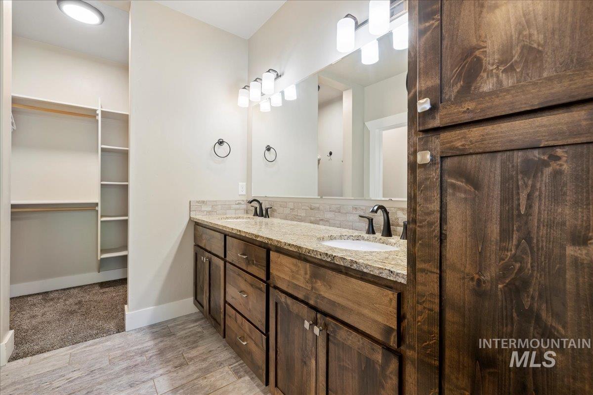 Bathroom featuring double vanity, decorative backsplash, wood finished floors, and a spacious closet