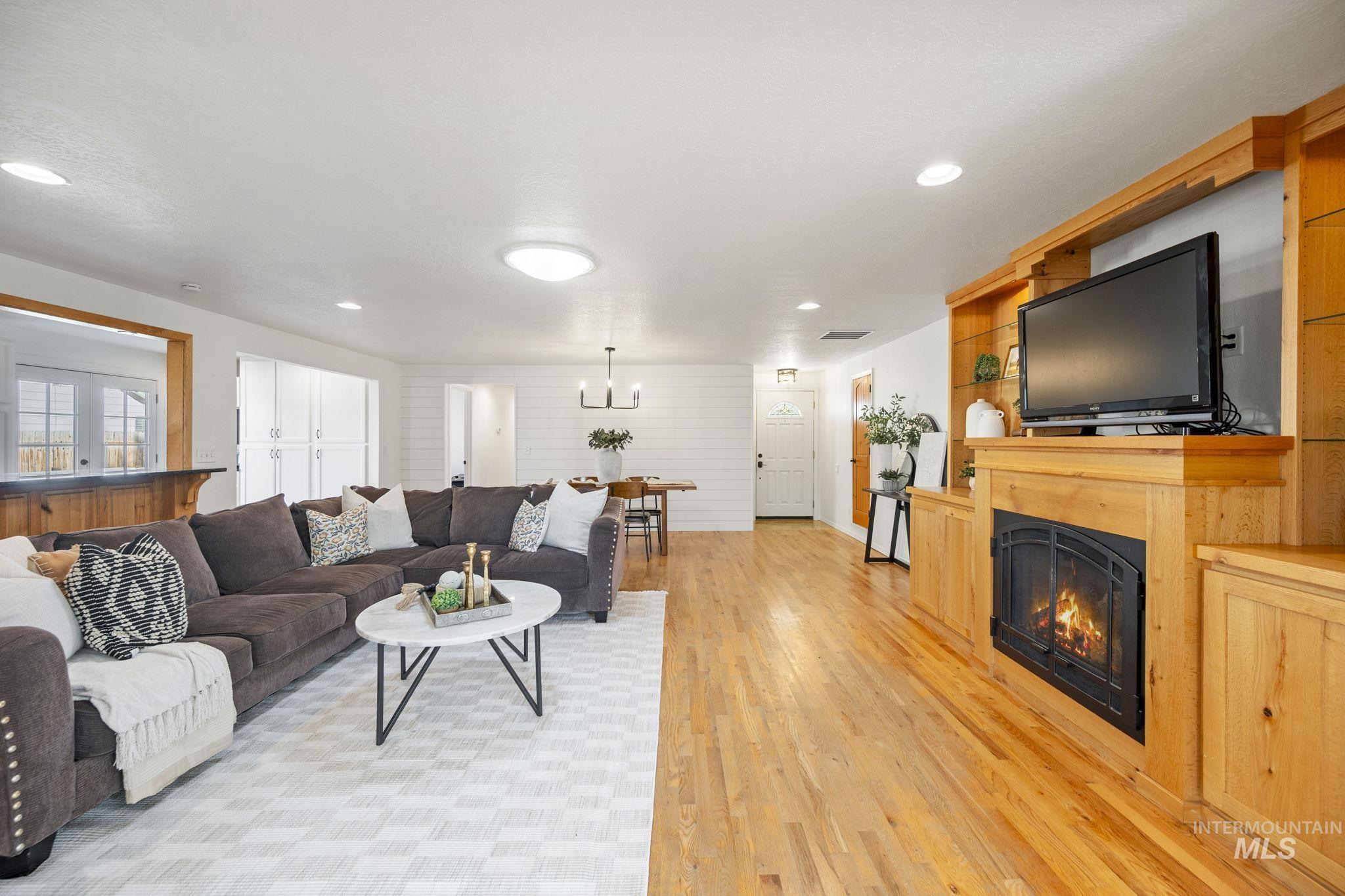 Living area featuring a glass covered fireplace, light wood finished floors, recessed lighting, and a chandelier