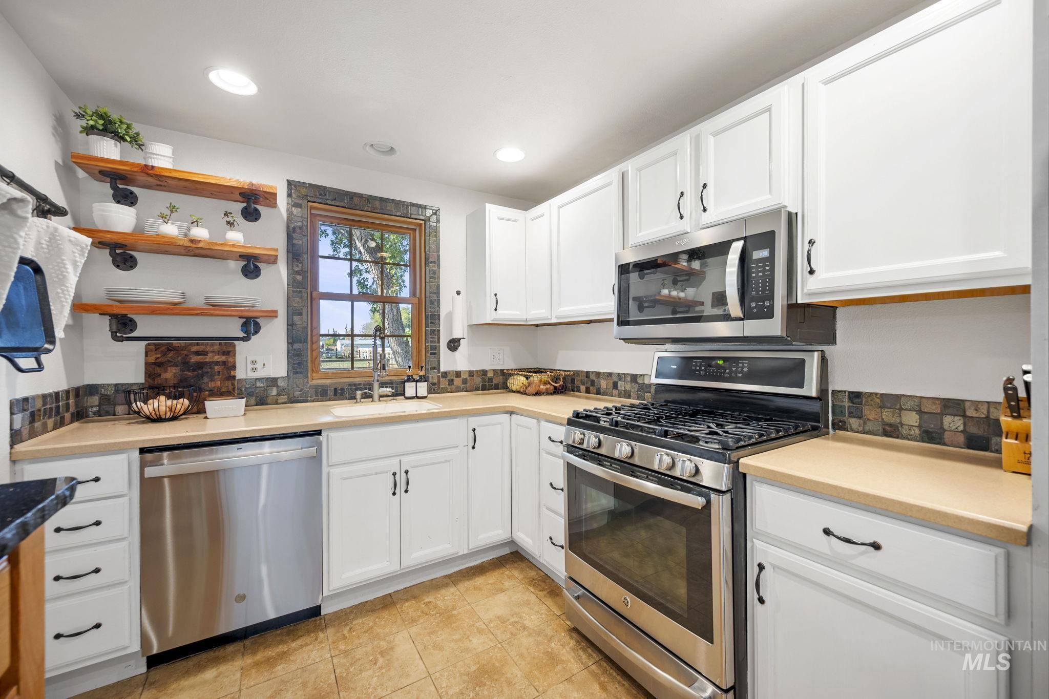 Kitchen featuring stainless steel appliances, open shelves, white cabinetry, light countertops, and tasteful backsplash