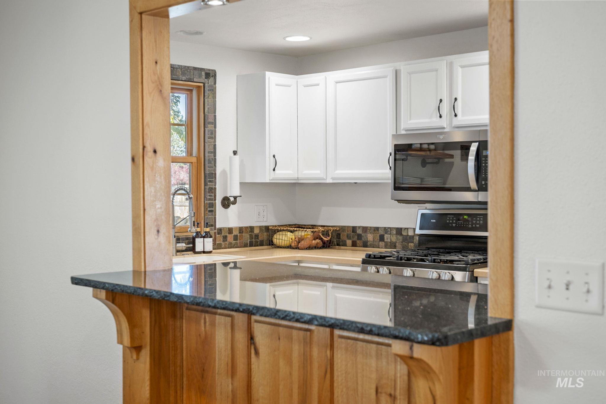 Kitchen with dark stone counters, white cabinetry, appliances with stainless steel finishes, and tasteful backsplash