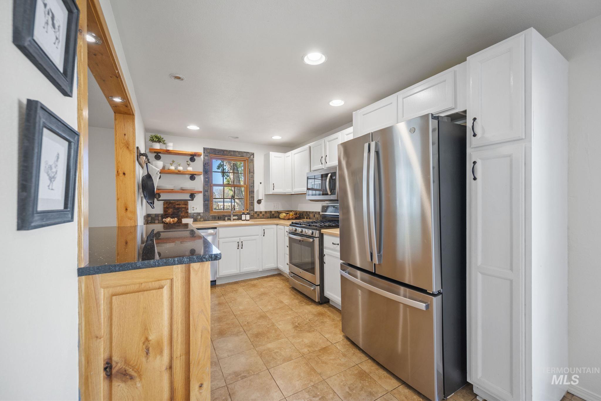 Kitchen featuring stainless steel appliances, open shelves, dark stone counters, recessed lighting, and white cabinetry