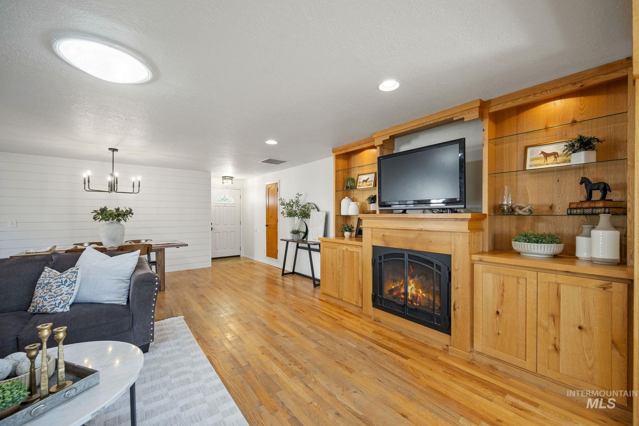 Living room with a lit fireplace, a textured ceiling, light wood-type flooring, a chandelier, and wood walls