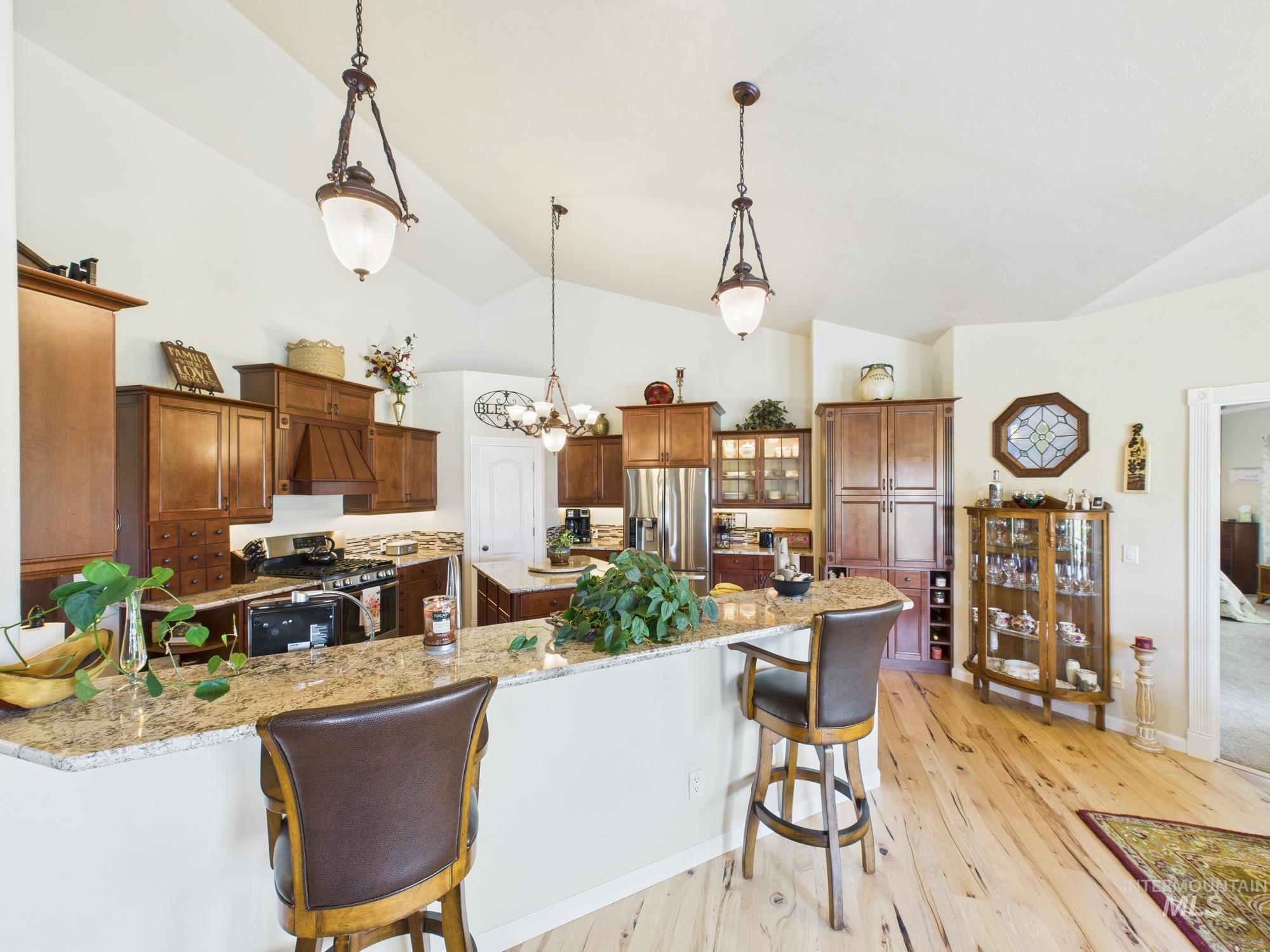 Kitchen featuring a breakfast bar area, decorative light fixtures, appliances with stainless steel finishes, light wood finished floors, and lofted ceiling