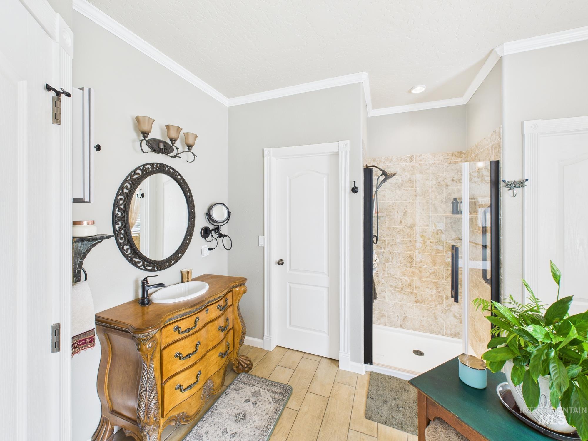 Bathroom with vanity, wood finish floors, a stall shower, and crown molding