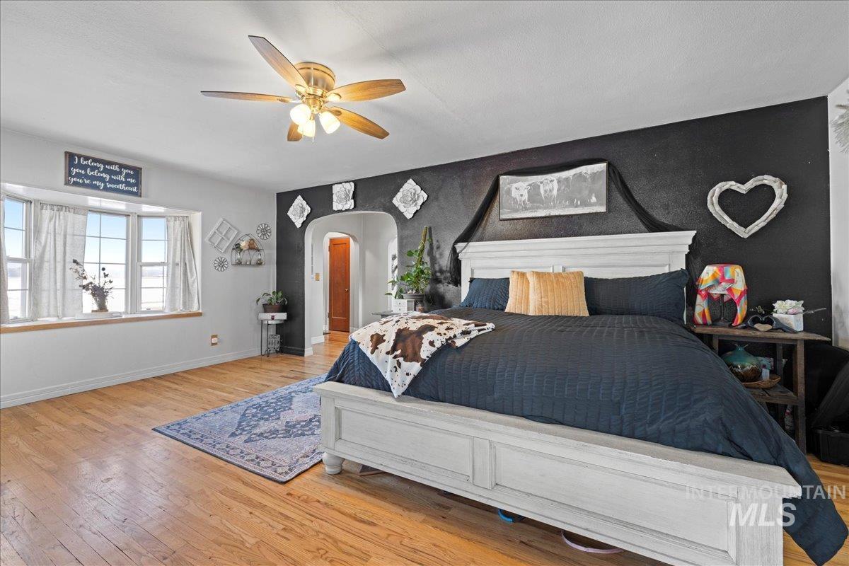 Bedroom featuring light wood-style flooring, arched walkways, a ceiling fan, and an accent wall