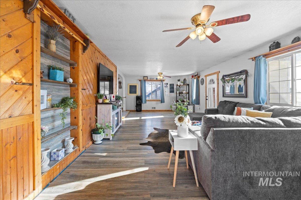 Living area featuring dark wood-style floors, a ceiling fan, a textured ceiling, and wood walls