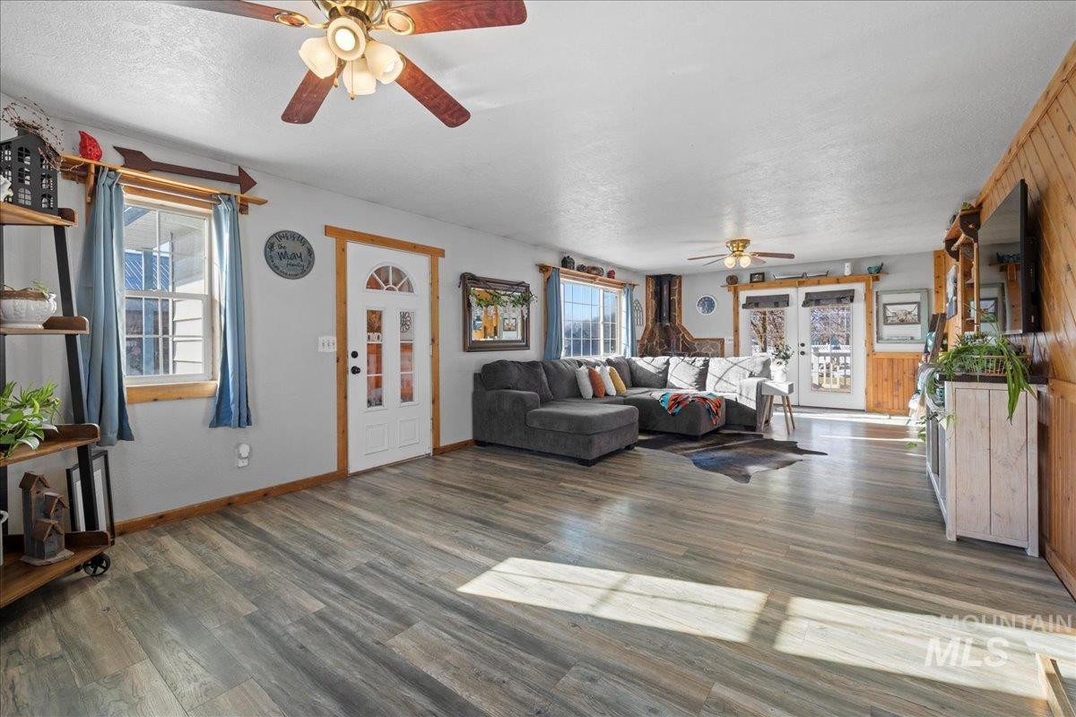 Living room featuring dark wood-style flooring, plenty of natural light, a textured ceiling, a ceiling fan, and wooden walls