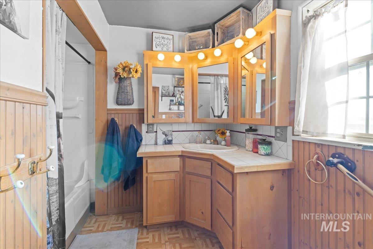Full bathroom with healthy amount of natural light, vanity, shower / tub combo with curtain, and wooden walls