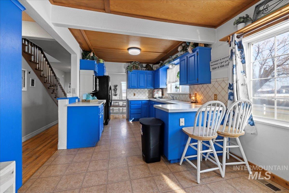 Kitchen with blue cabinetry, a peninsula, light countertops, a breakfast bar area, and tasteful backsplash