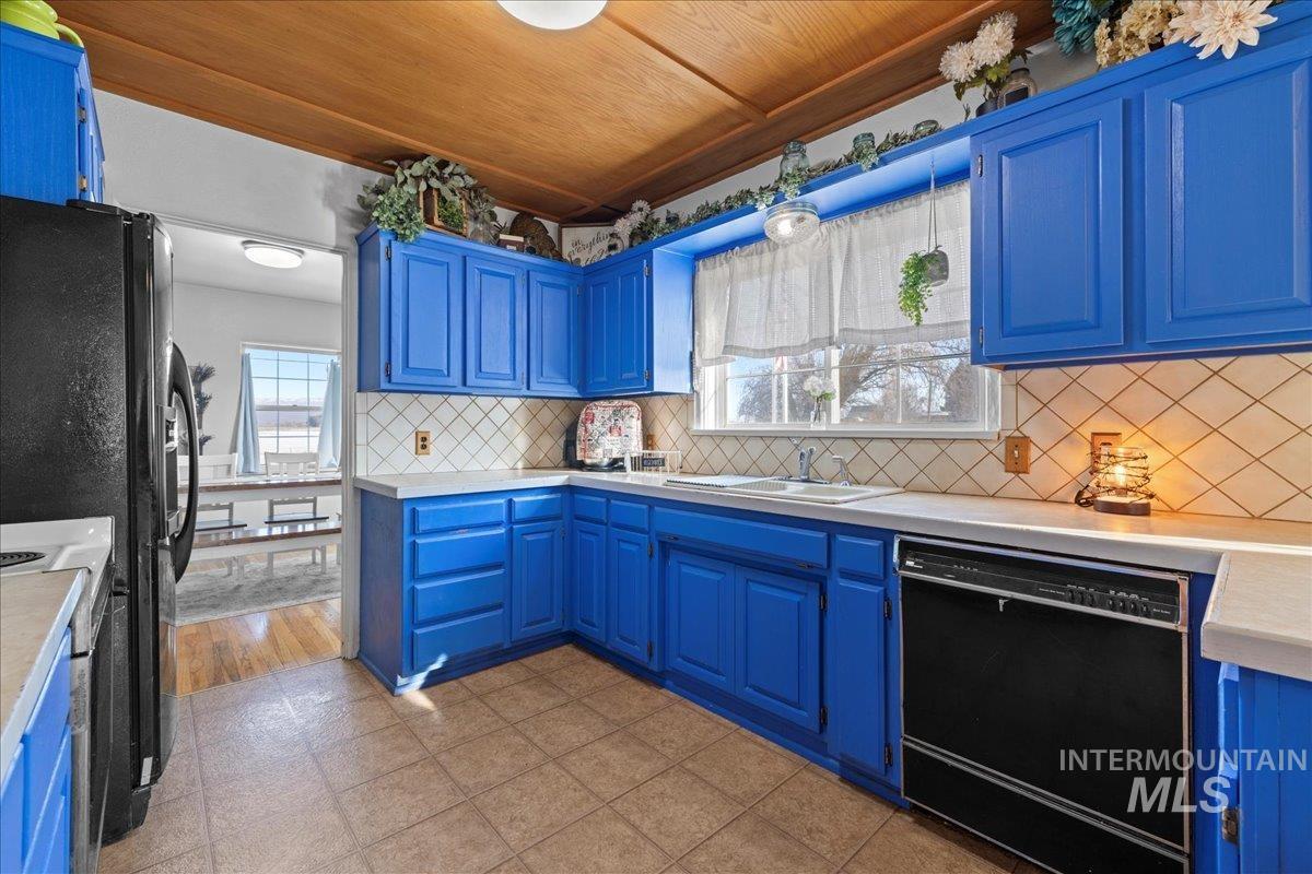 Kitchen with blue cabinetry, light countertops, black appliances, decorative backsplash, and wood ceiling