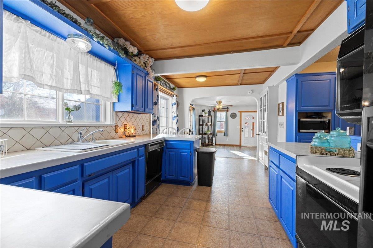Kitchen featuring light countertops, blue cabinets, decorative backsplash, arched walkways, and a wood ceiling with exposed beams