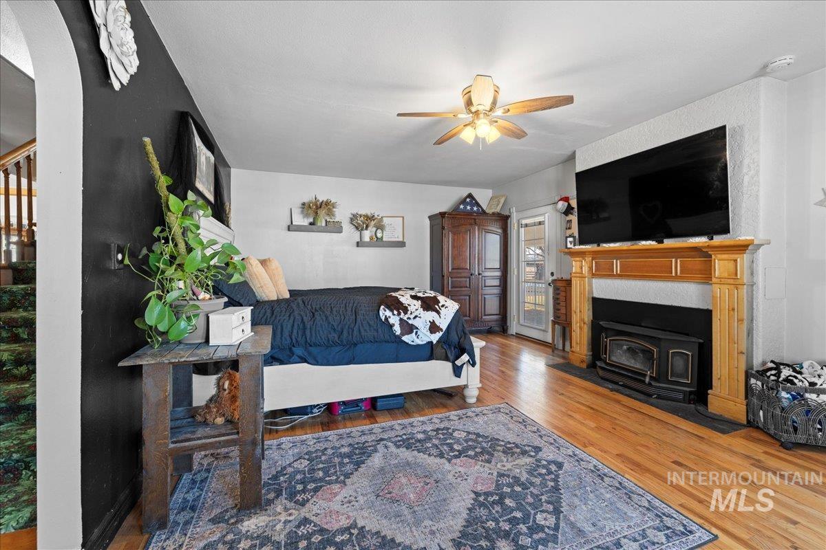 Living area with wood finished floors, stairway, a wood stove, arched walkways, and ceiling fan