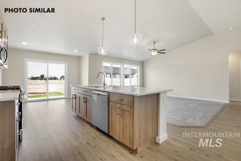 Kitchen with decorative light fixtures, stainless steel appliances, a kitchen island with sink, brown cabinets, and open floor plan