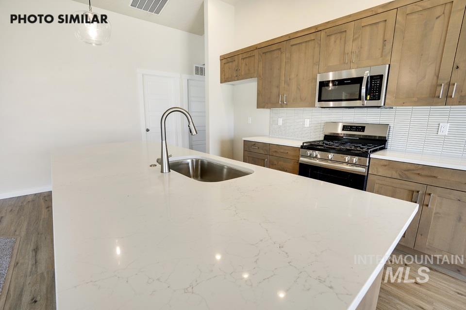 Kitchen featuring light wood-type flooring, appliances with stainless steel finishes, decorative backsplash, and light stone countertops