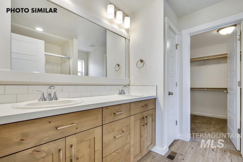 Full bath featuring double vanity, light wood finished floors, a shower stall, and a walk in closet