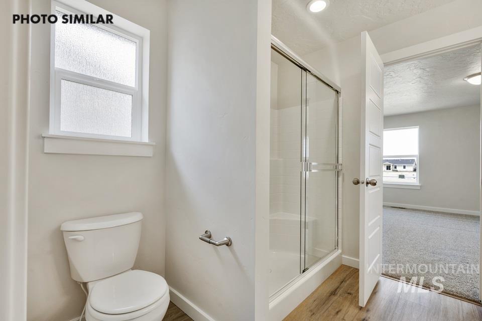 Bathroom with a textured ceiling, light wood-style floors, and a shower stall