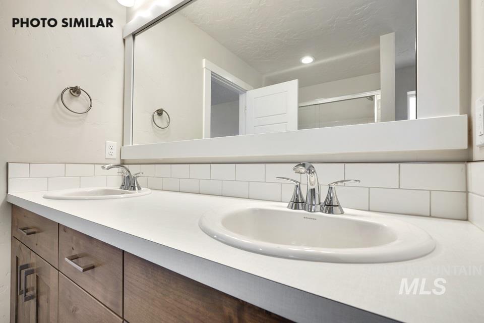Bathroom with double vanity, a shower stall, backsplash, and a textured ceiling