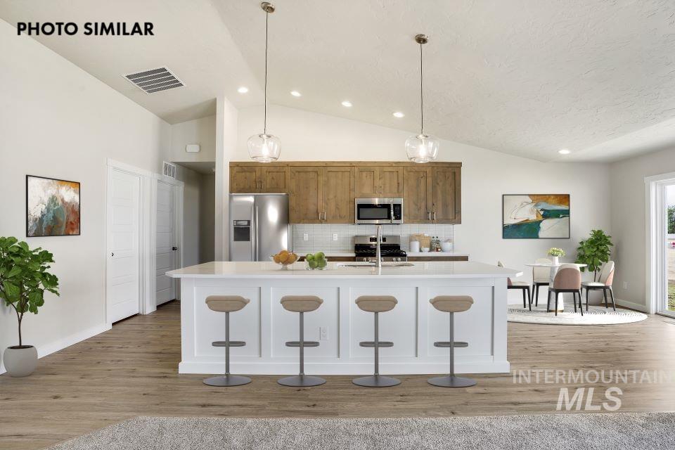 Kitchen with lofted ceiling, tasteful backsplash, stainless steel appliances, pendant lighting, and a breakfast bar