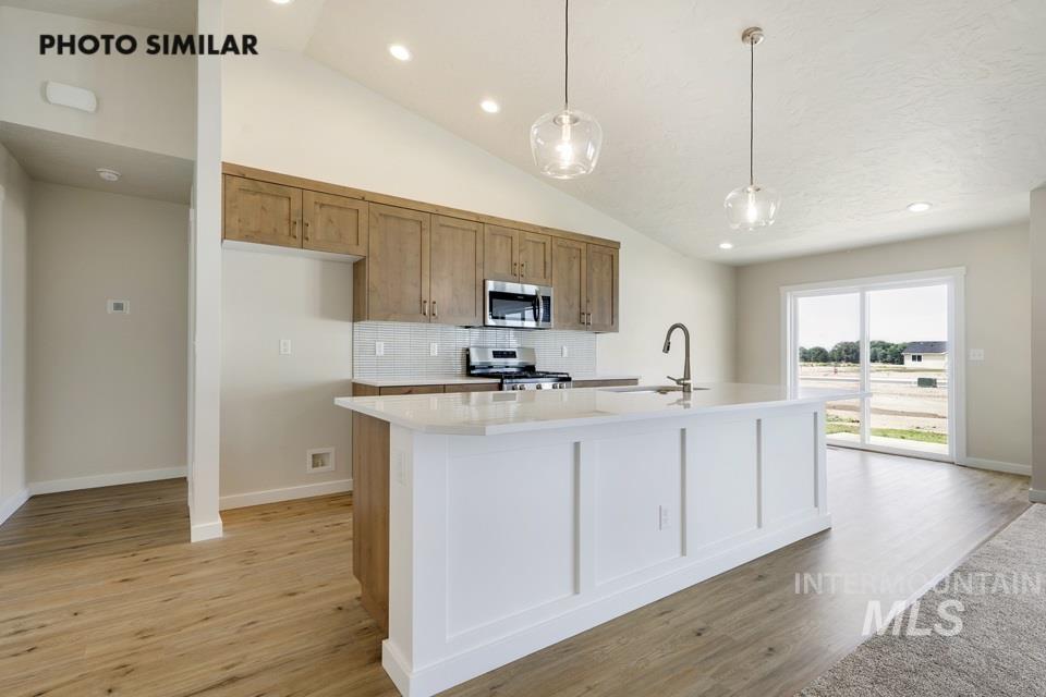 Kitchen featuring tasteful backsplash, decorative light fixtures, light stone counters, recessed lighting, and a kitchen island with sink