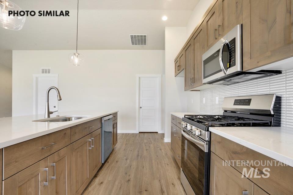 Kitchen with stainless steel appliances, light wood-style flooring, hanging light fixtures, light stone countertops, and recessed lighting