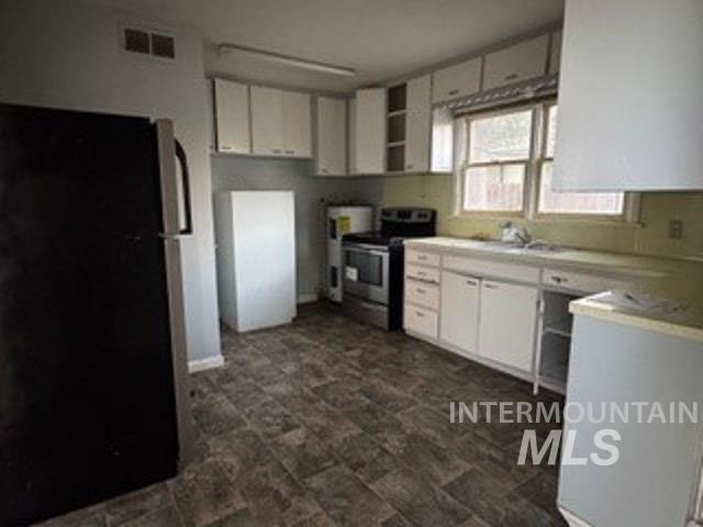 Kitchen with appliances with stainless steel finishes, white cabinetry, light countertops, and stone finish floors