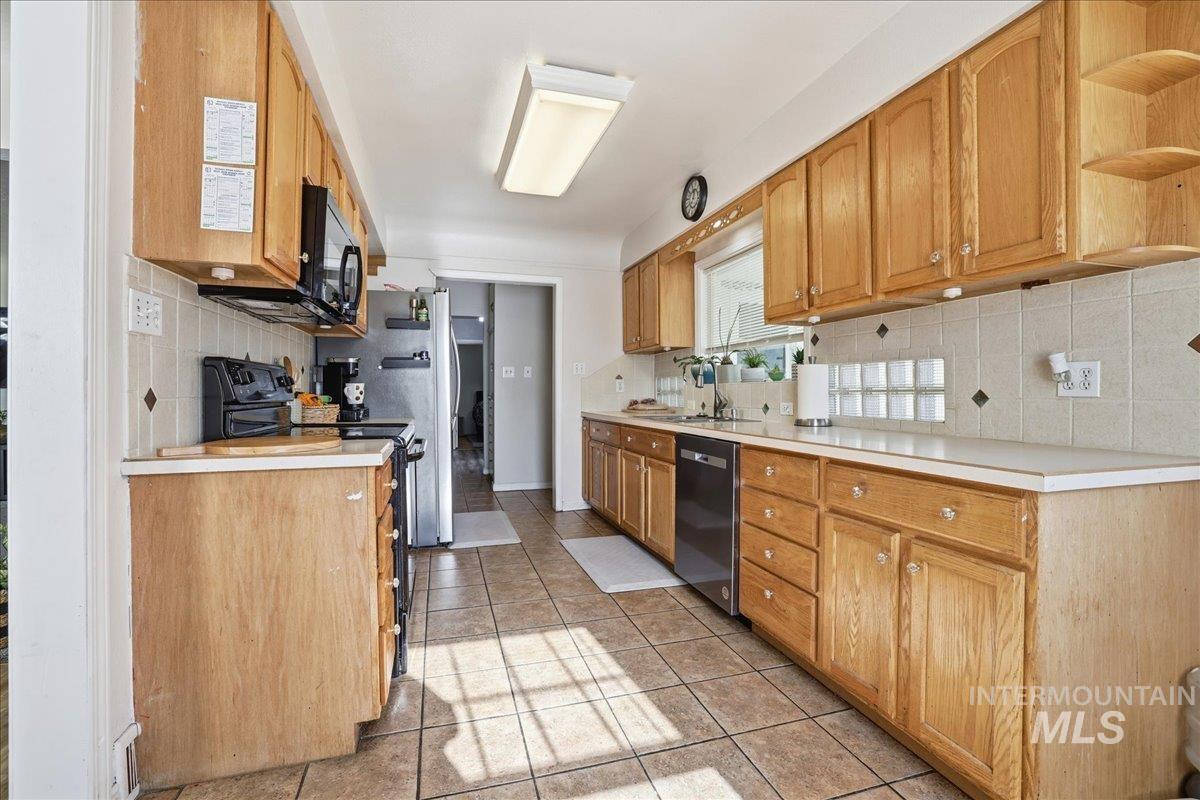 Kitchen with light countertops, backsplash, black appliances, light tile patterned flooring, and open shelves