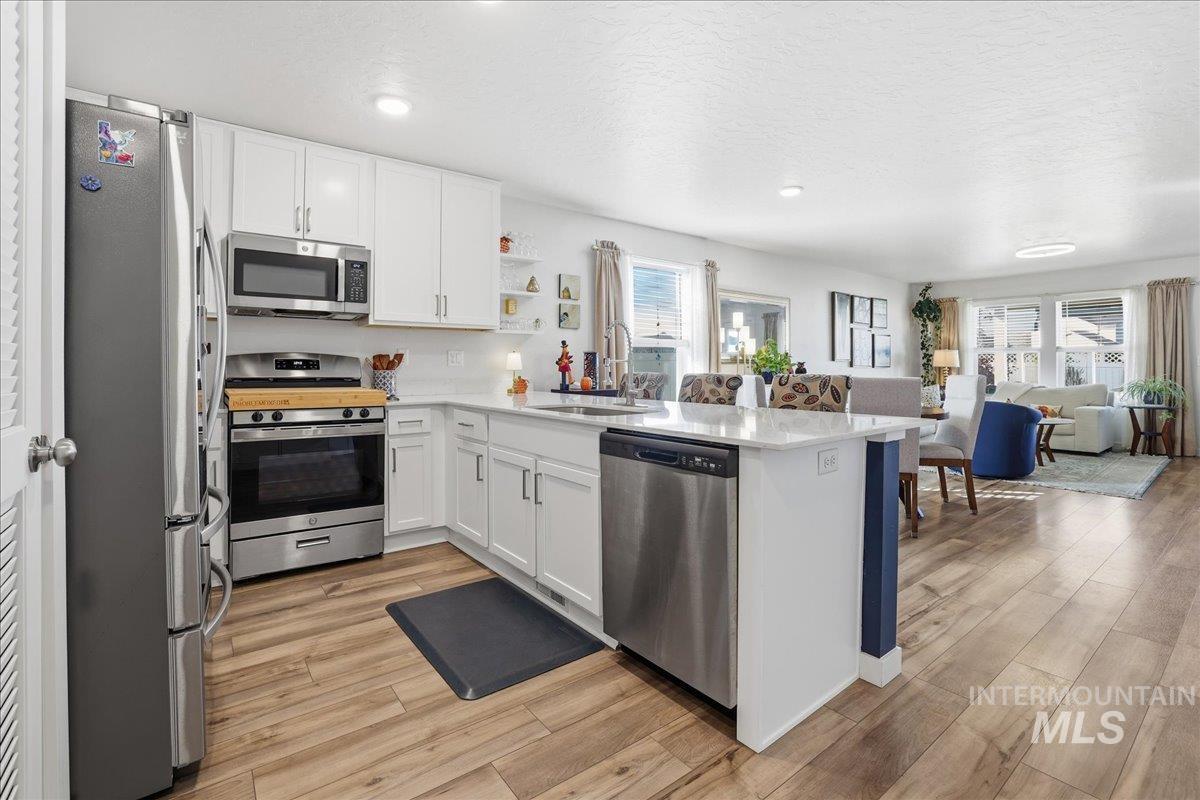 Kitchen featuring open floor plan, stainless steel appliances, white cabinets, a peninsula, and a textured ceiling