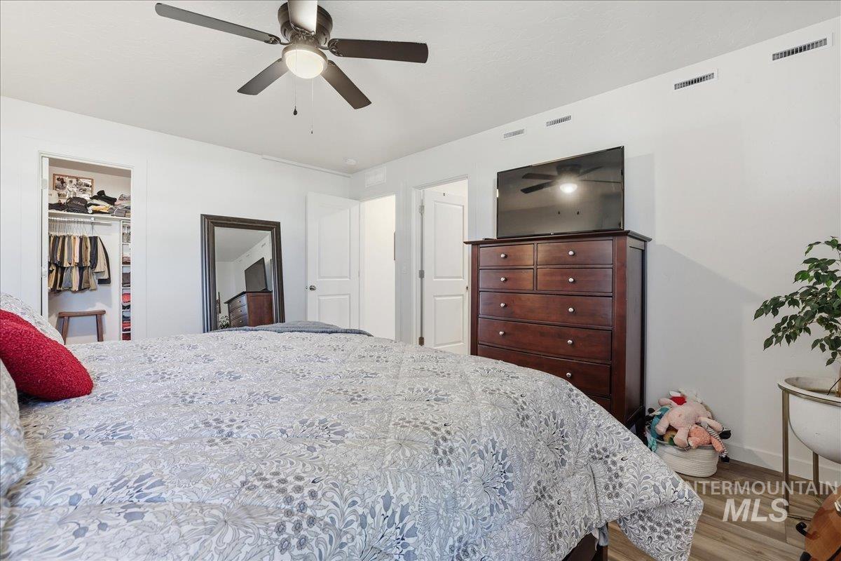 Bedroom with wood finished floors, a spacious closet, and a ceiling fan