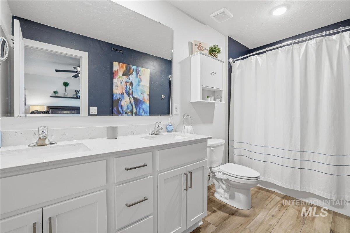 Ensuite bathroom with light wood-style floors, double vanity, and a textured ceiling