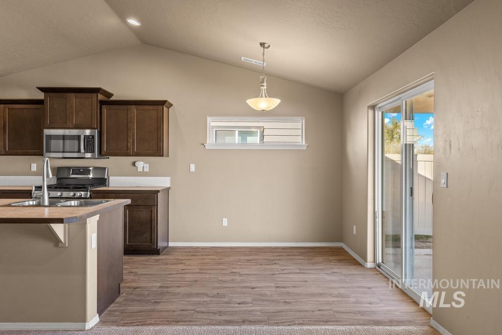 Kitchen with a breakfast bar area, vaulted ceiling, stainless steel appliances, dark brown cabinetry, and light countertops