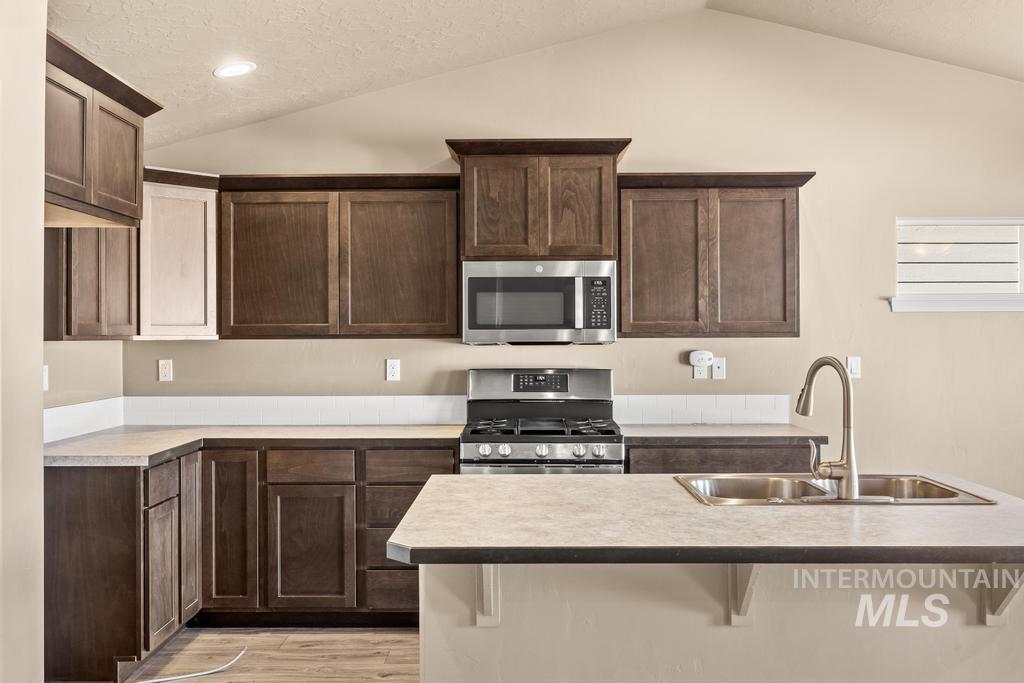 Kitchen with stainless steel appliances, dark brown cabinets, a textured ceiling, lofted ceiling, and light countertops