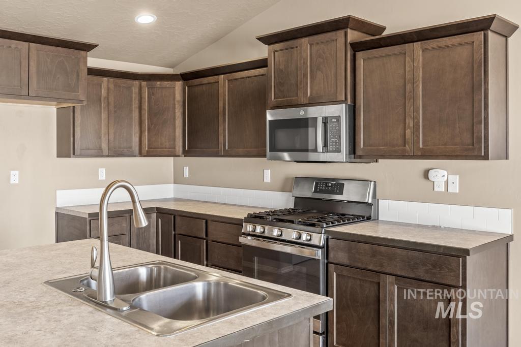 Kitchen with light countertops, dark brown cabinetry, lofted ceiling, stainless steel appliances, and recessed lighting